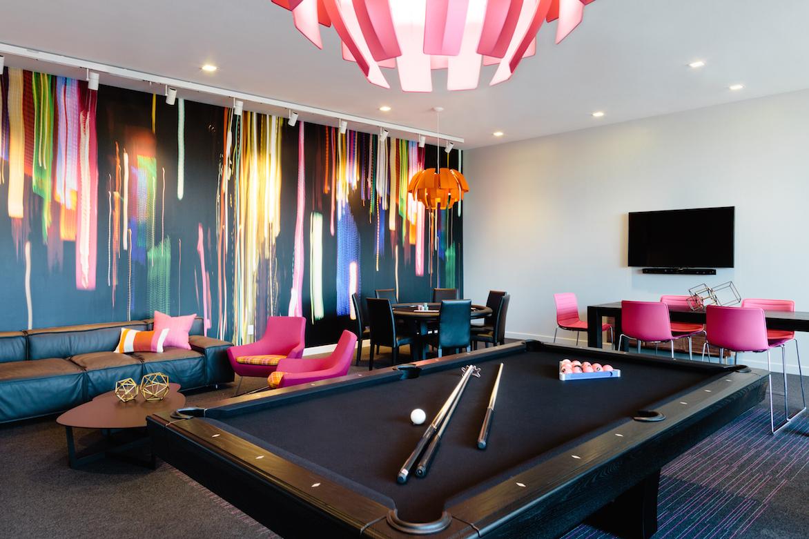 Pool table and lounge area with couches, a poker table, floor to ceiling abstract wall mural and wall-mounted TV