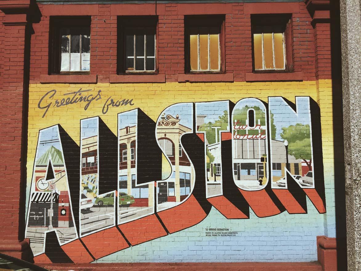 "Greetings from Allston" painted on the side of a building in the style of a vintage "greetings from" post card