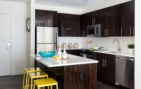 View of Contunuum North kitchen with island eating area, stainless steel appliances and dark wooden cabinets and accents