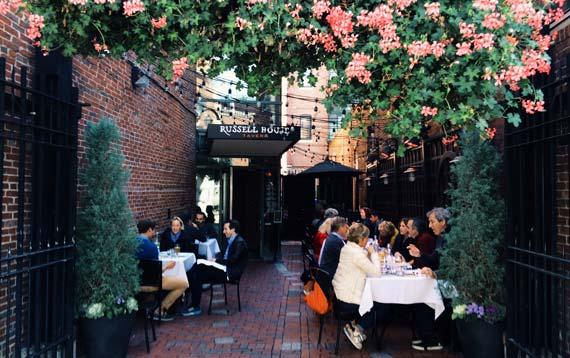 Secluded alley seating area for the Russell House Tavern with 7 tables. Area decorated with ivy and shrubs.